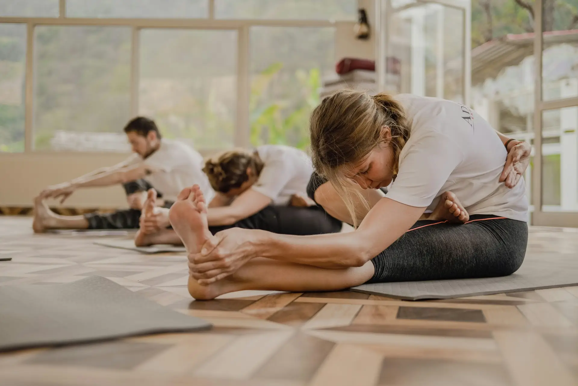 Três pessoas durante um exercício de alongamento numa aula de pilates